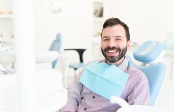 A cheerful middle-aged man with a perfect smile sitting in in a dental chair.