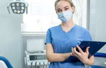 A female dental care professional wearing a surgical mask in a dental treatment room.