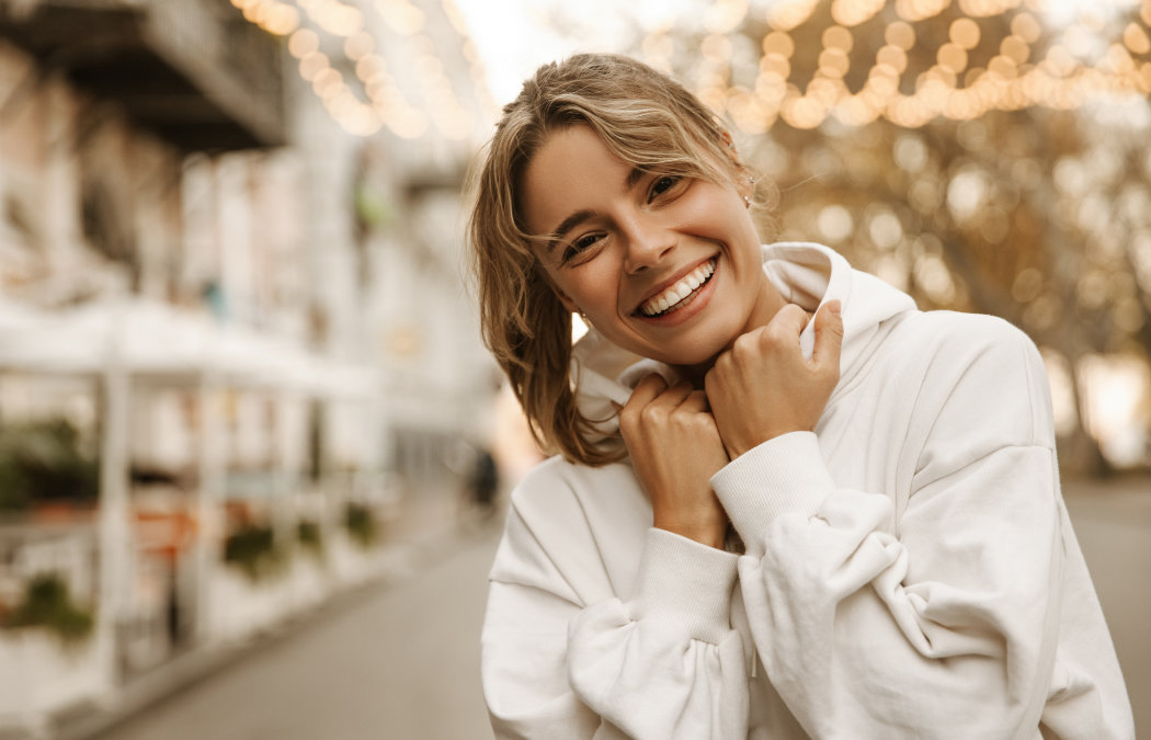 Person in a white hoodie smiling outdoors, with blurred lights and buildings in the background., Indian Land, SC