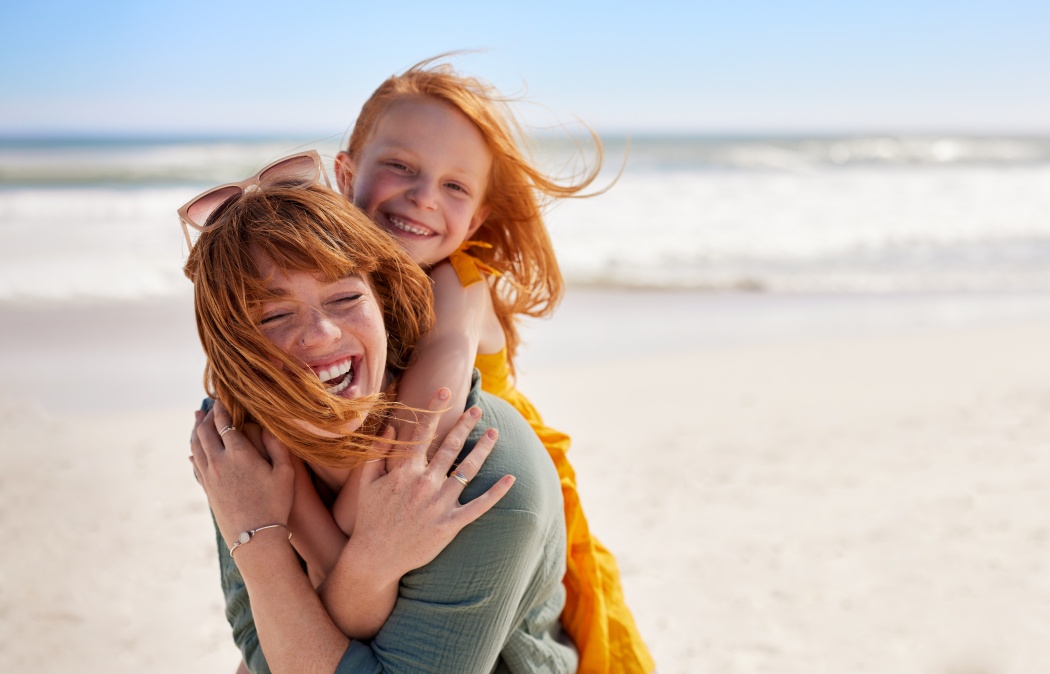 Smiling mother and beautiful daughter having fun at the beach. Portrait of happy woman giving a piggyback ride to cute little girl with copy space. Portrait of happy red hair kid embracing her mom., Indian Land, SC